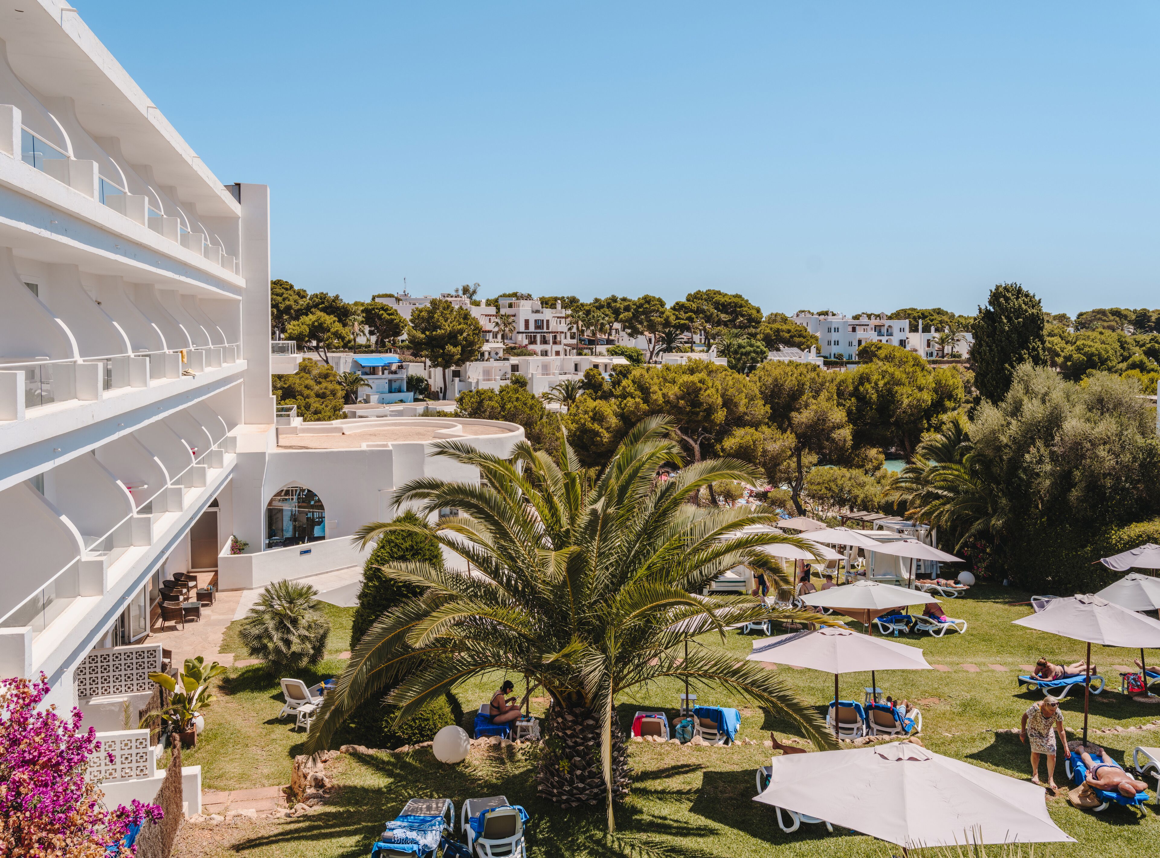 A resort with a pool area, sun loungers, and a view of the surrounding buildings and greenery.