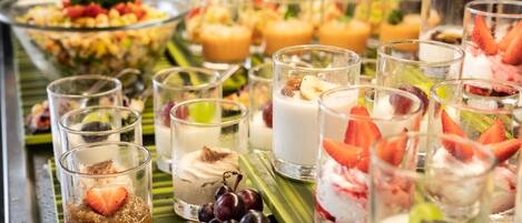 Un bufé con diversas opciones de comida y bebida, incluyendo frutas, postres y refrescos.
