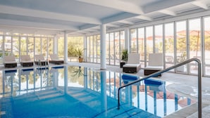 An indoor swimming pool with clear blue water, surrounded by white columns and large windows offering views of the outdoors. - Grupotel Rocador (Santanyi)