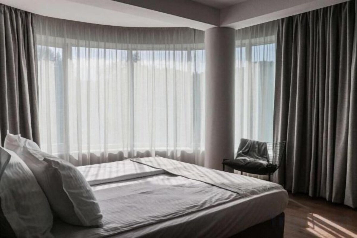 Habitación de hotel con una cama grande, una silla y vistas a través de cortinas translúcidas.