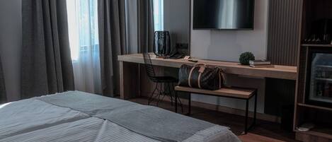 A hotel room with a bed, a desk with a chair, a television, and a minibar.