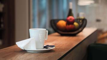 Una taza blanca con una servilleta sobre una mesa de madera, un cuenco de fruta al fondo y una botella de vino.