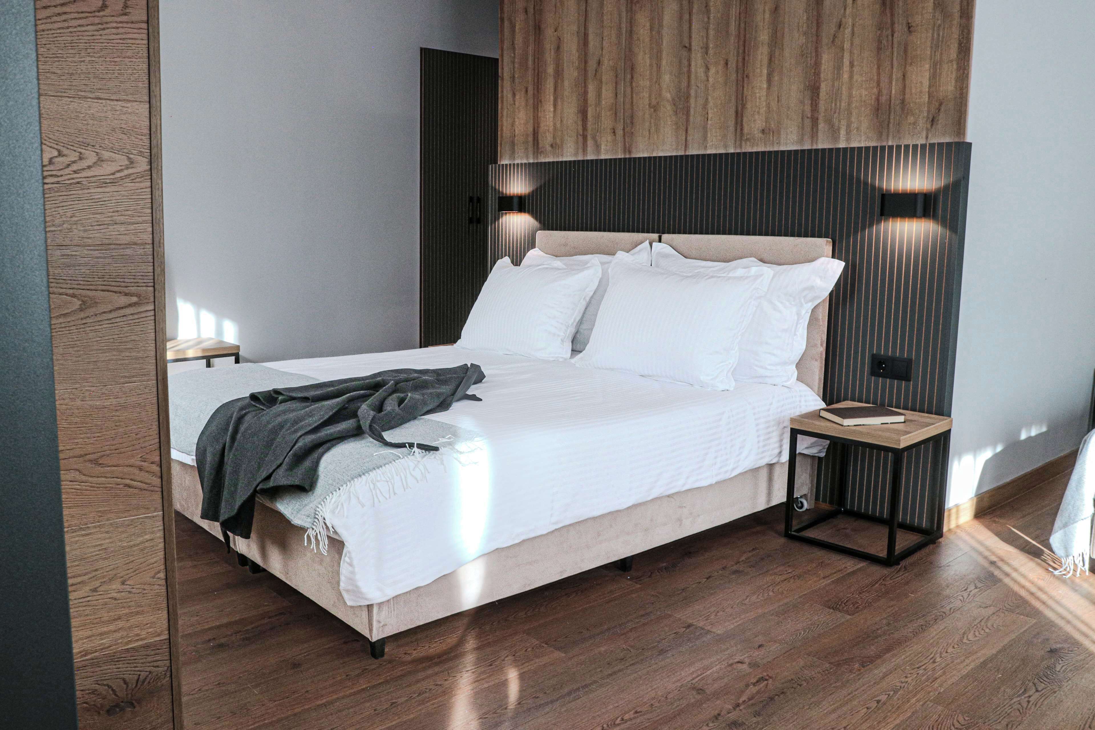 Un dormitorio moderno con cabecera de cama de madera, ropa de cama blanca y dos lámparas de noche.