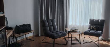 Una habitación moderna con dos sillas tapizadas en negro, una mesita de madera y un bolso de cuero negro sobre una estantería.