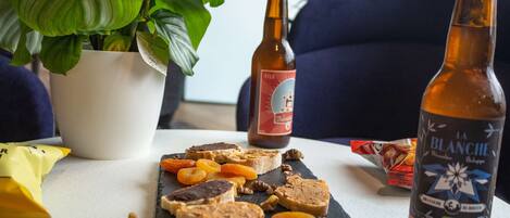 Una mesa con una botella de vino La Blanche, una botella de cerveza y una pizarra con diversos aperitivos.