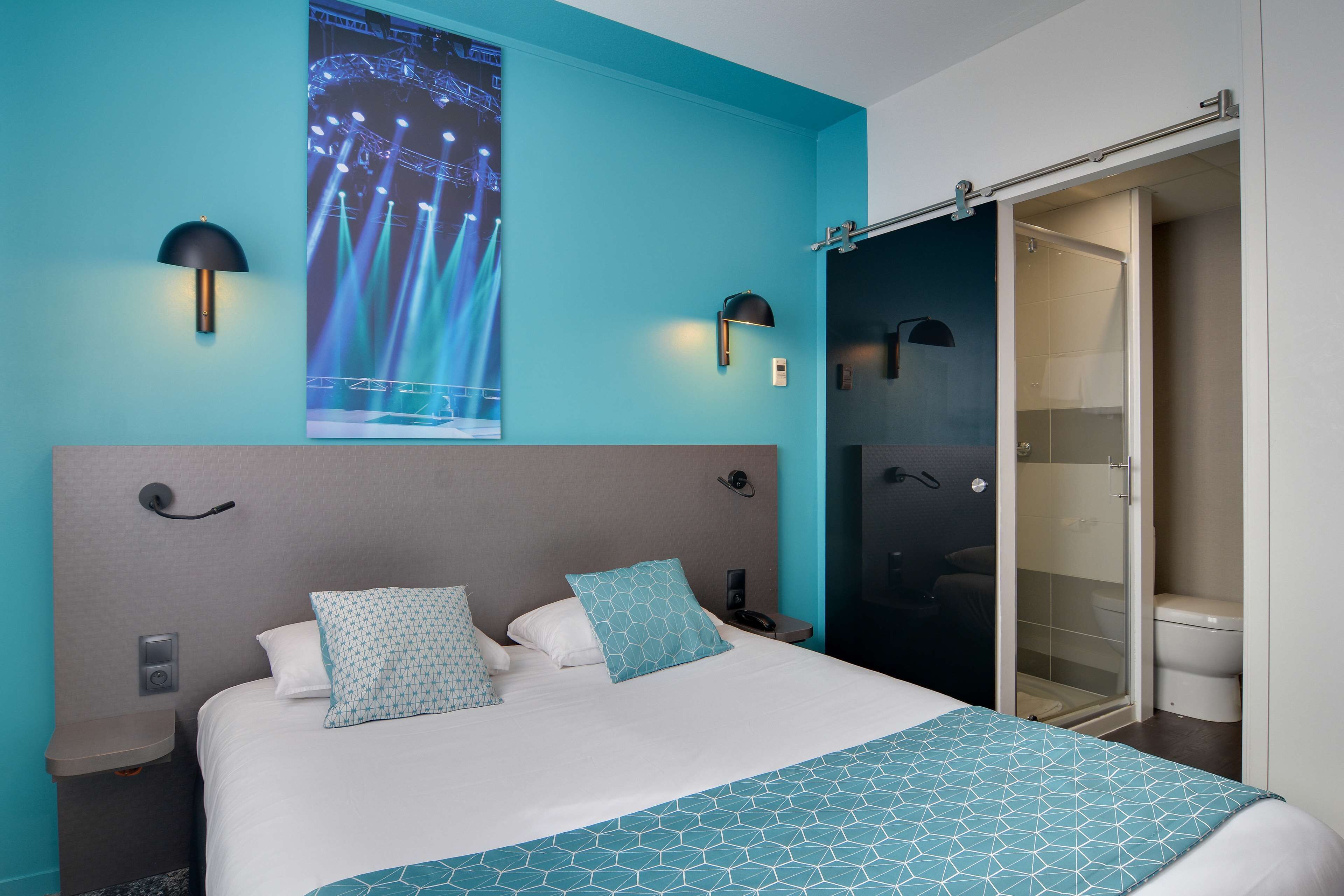 A modern hotel room with a large bed, a shower area, and a wall-mounted TV displaying a concert.