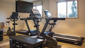 Un gimnasio con cintas de correr, bicicletas estáticas y un banco de pesas.