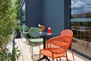 Un patio al aire libre con sillas verdes y naranjas, una mesa y un vaso de bebida roja.