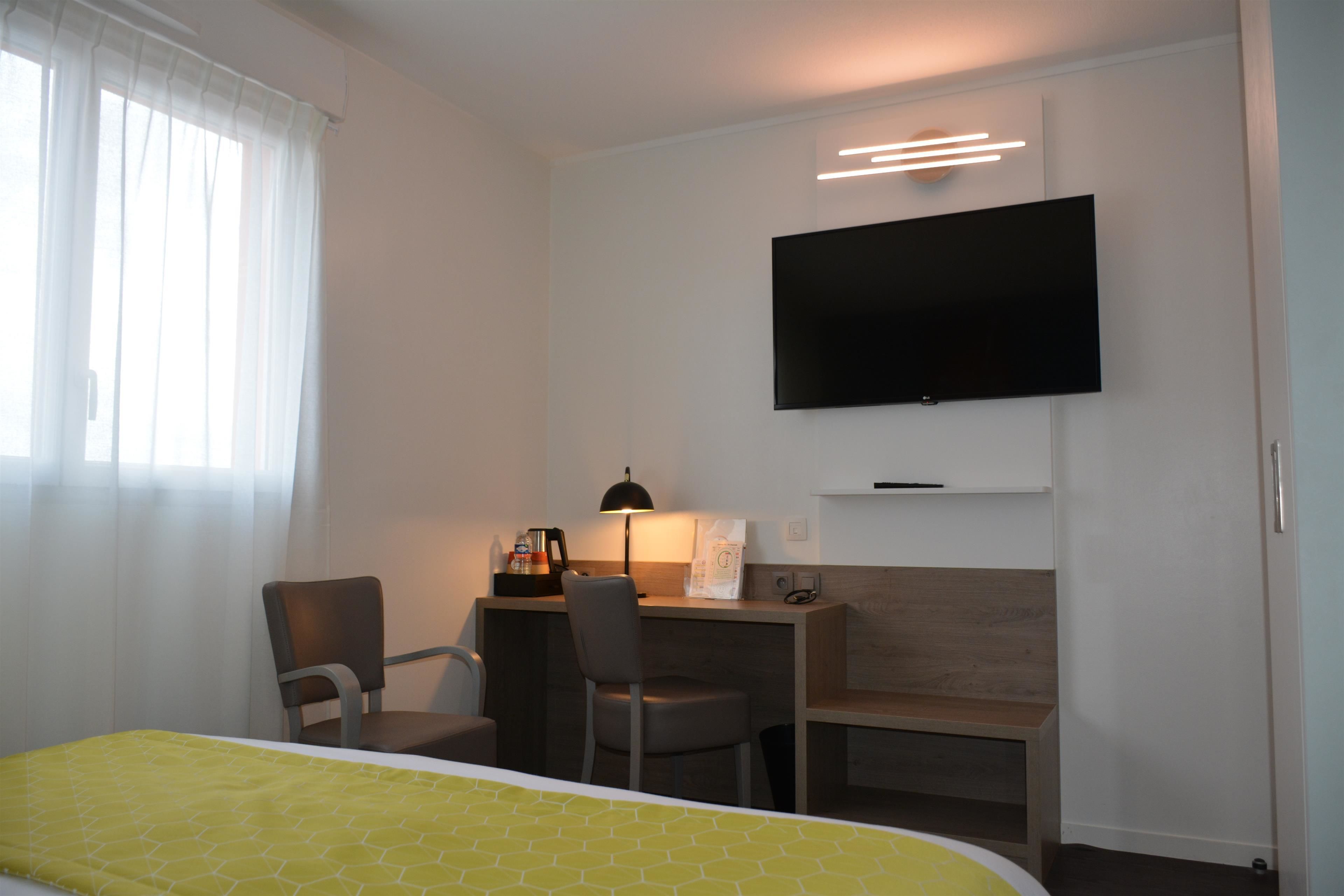 Une chambre d’hôtel équipée d’un lit, d’un bureau, d’une chaise, d’une télévision et d’une fenêtre avec des rideaux.