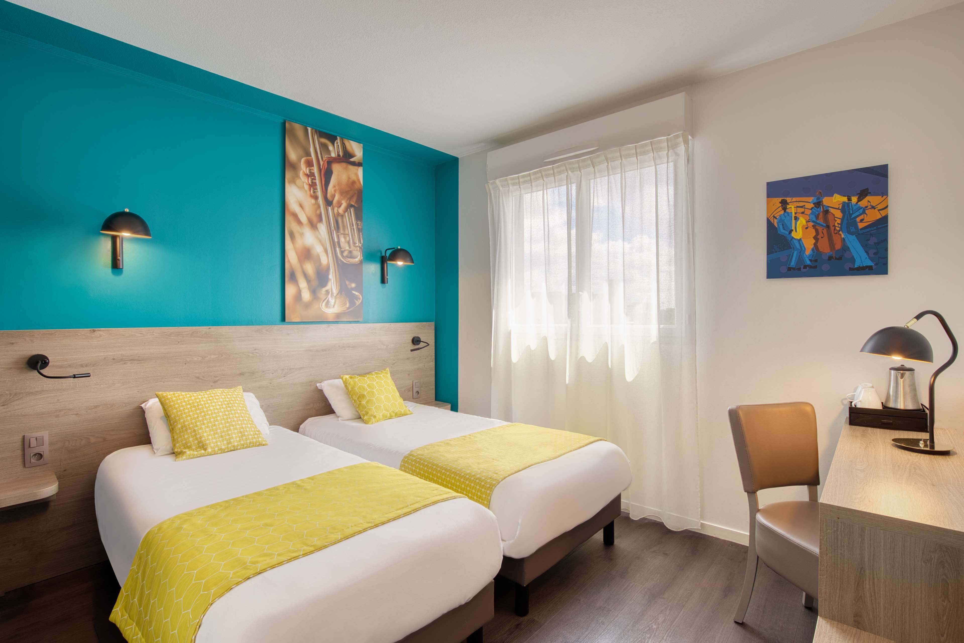 Ein Hotelzimmer mit zwei Betten, einem Schreibtisch, einem Stuhl, einem Fenster mit Vorhängen und Bildern an den Wänden.