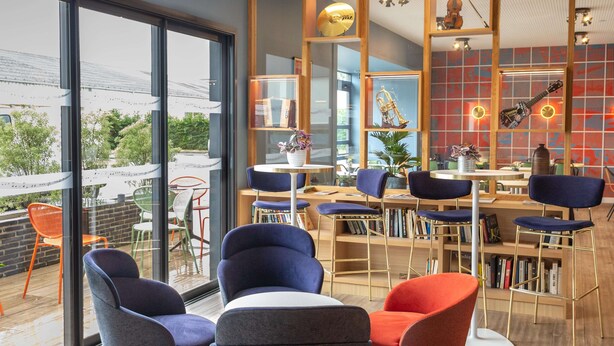 Un interior moderno con un ventanal grande, una estantería de madera y un comedor con sillas y mesas.