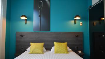 A hotel room with a large bed, two bedside lamps, a mounted microphone, and a nightstand with a phone.