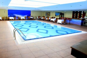 A swimming pool with a tiled deck, a bar area with chairs, and a mural on the wall.
