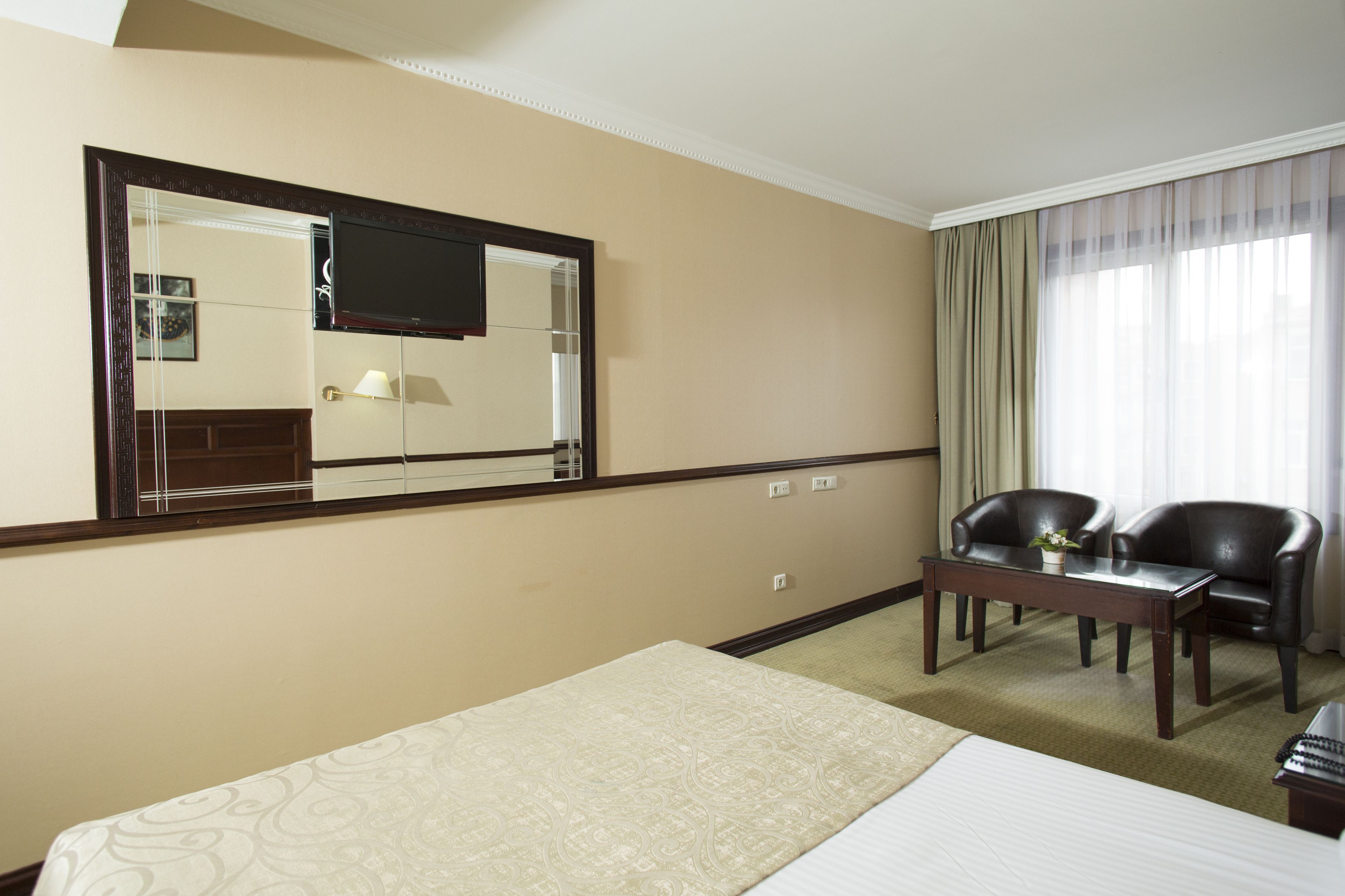 A hotel room with a bed, a desk, two chairs, a television, and a large window with curtains.