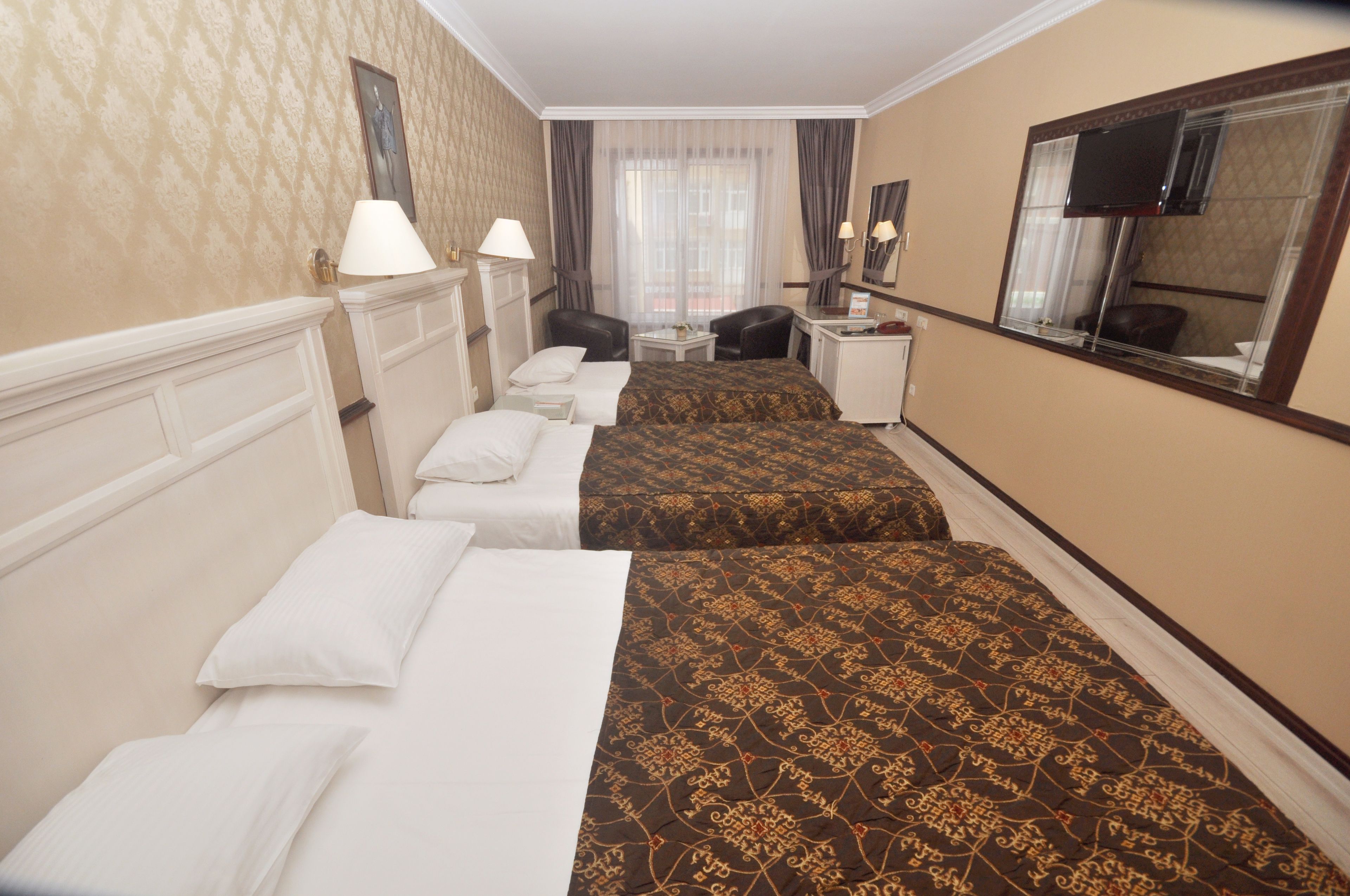 A hotel room with two beds, a desk, a chair, a TV, and a window with curtains.
