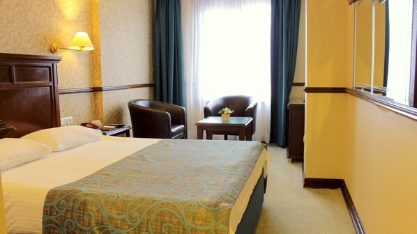 A hotel room with a large bed, a desk, a chair, and a lamp.