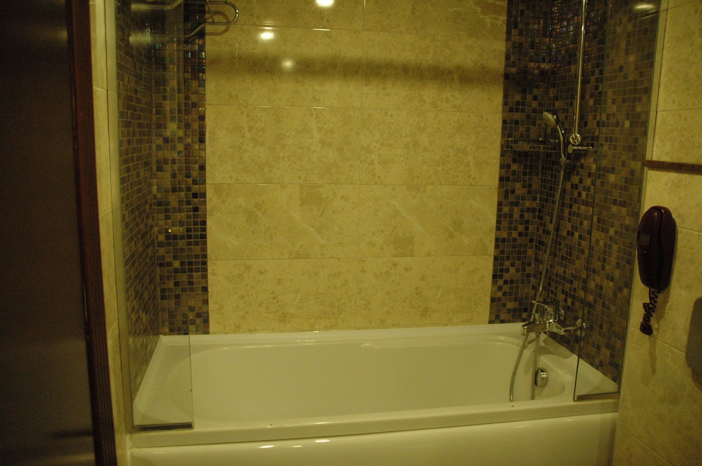 Casa de banho com chuveiro em cabine de vidro, banheira branca e paredes com azulejos mosaicos.