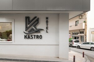 Un letrero de hotel con un logotipo estilizado y el nombre "KASTRO HOTEL" en una pared blanca.