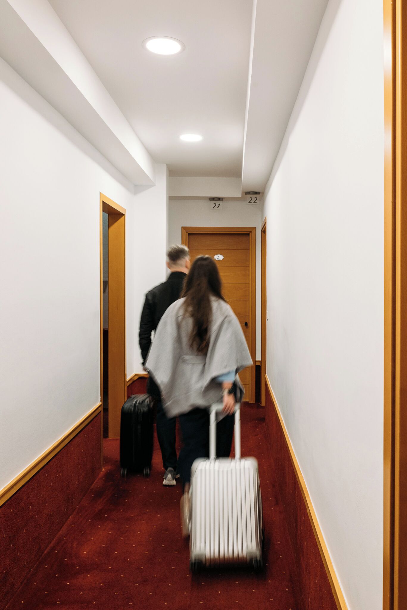 A narrow hallway with white walls and a red carpet, leading to a wooden door marked with the number 22.