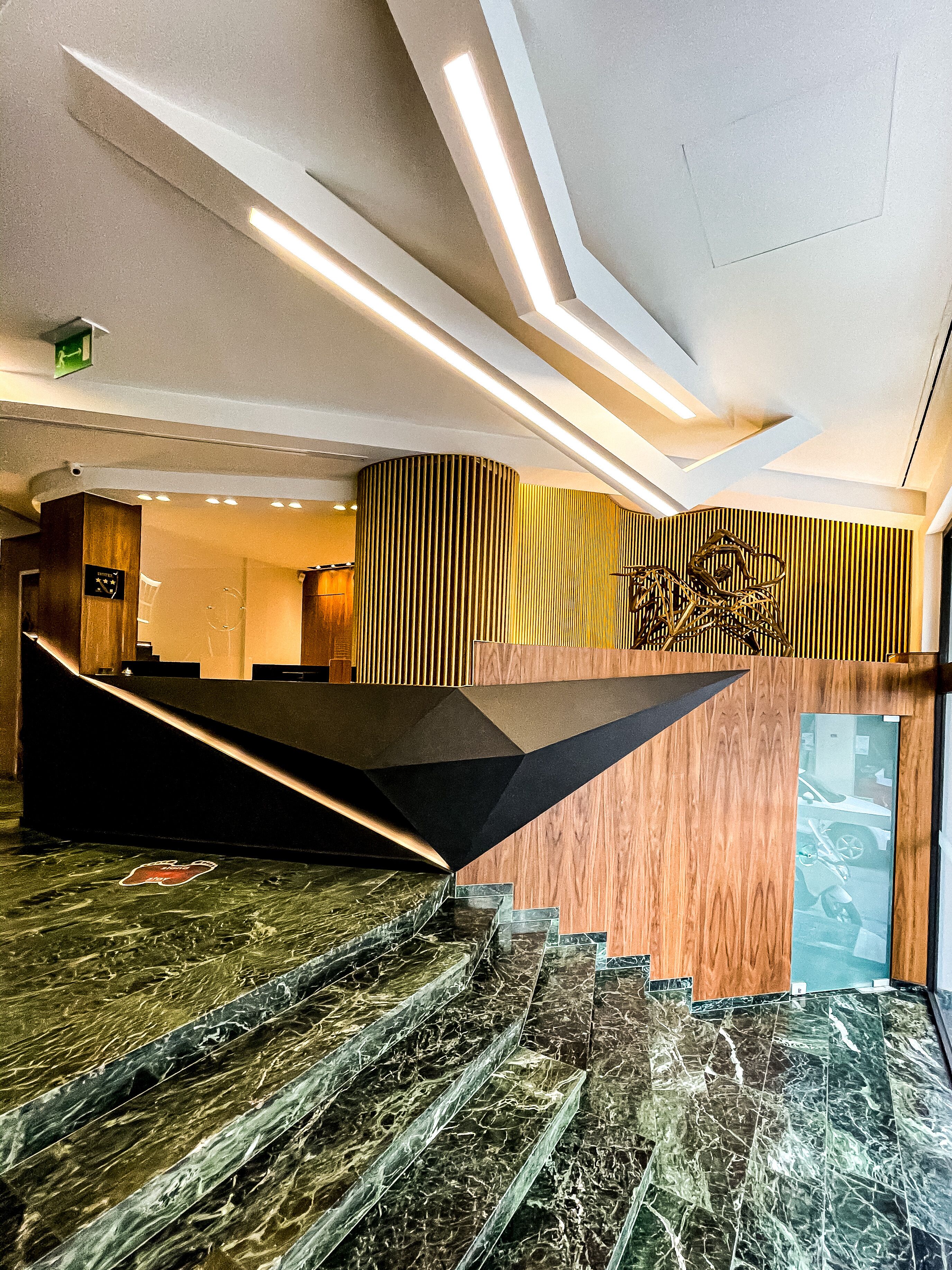 A modern hotel lobby with a marble staircase, wooden paneling, and a reception desk.
