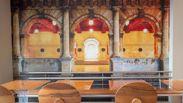 A dining area with a mural of an arched passageway, wooden tables, and chairs. - Kastro Hotel (Heraklion)