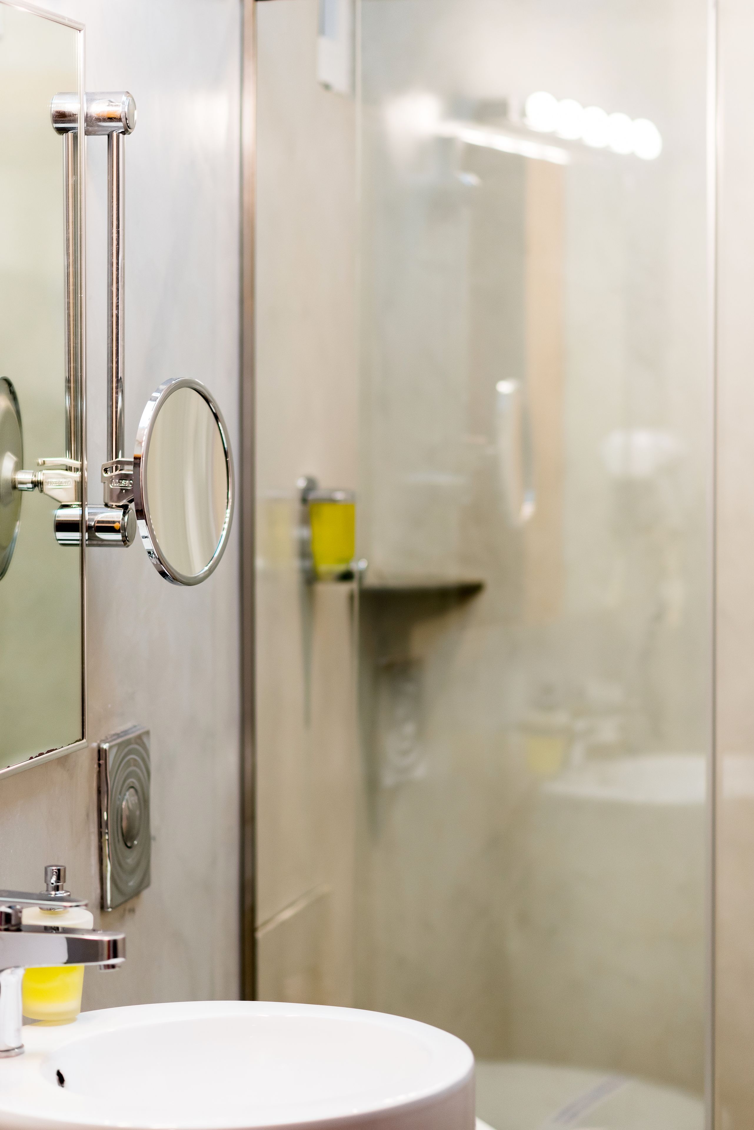 A bathroom with a round mirror, a sink, and a glass shower enclosure.