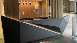 A modern reception desk with a wooden panel design, a logo, and a digital clock display. - Kastro Hotel (Heraklion)