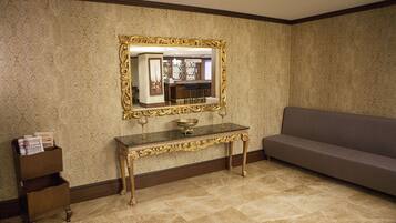 Una habitación con un espejo de marco dorado, suelo de baldosas de mármol, un sofá y una pequeña mesita de madera con revistas.