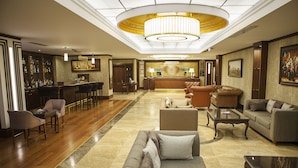 Um hall de hotel com balcão de recepção, área de bar, assentos e um candelabro.