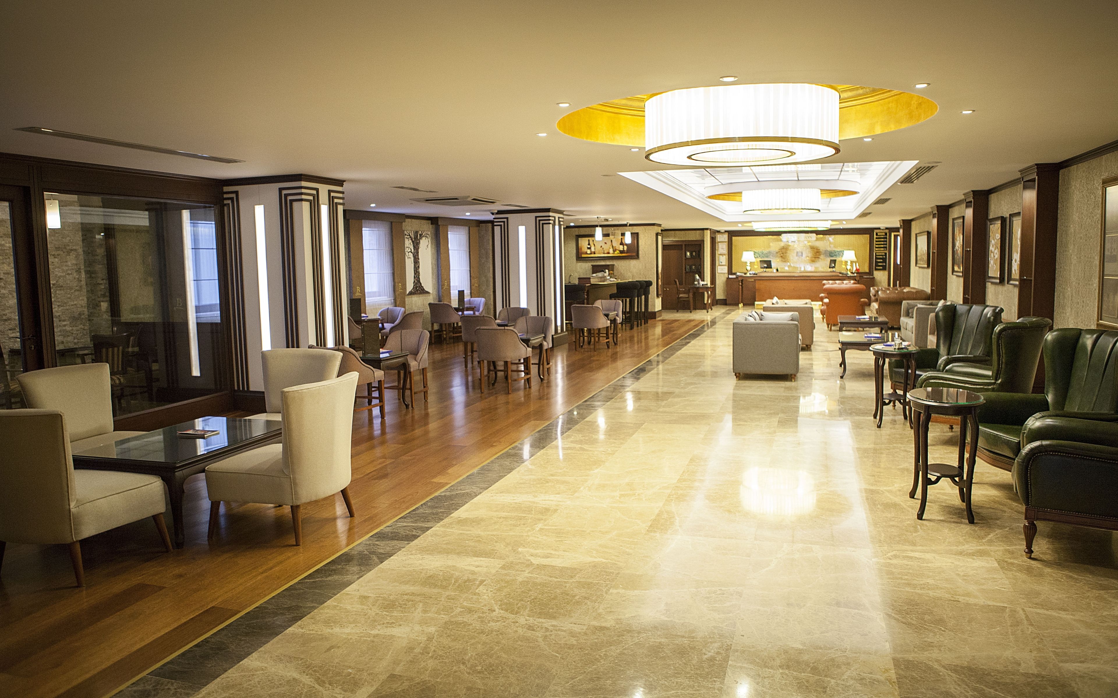 Un hall d’entrée spacieux avec un long comptoir de réception, plusieurs espaces de détente dotés de fauteuils et de canapés, et un grand lustre.