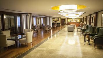 Un hall d’entrée spacieux avec un long comptoir de réception, plusieurs espaces de détente dotés de fauteuils et de canapés, et un grand lustre.