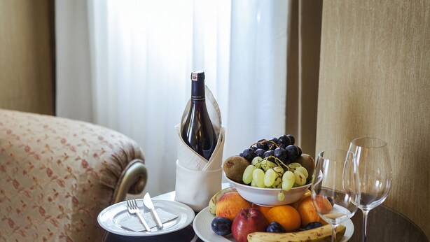 Uma mesa com uma garrafa de vinho, uma tigela de frutas e dois copos de vinho.