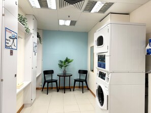 A laundry room with a washing machine, two chairs, a small table, and a potted plant. - Holiday Inn Express Causeway Bay Hong Kong by IHG (Hong Kong)