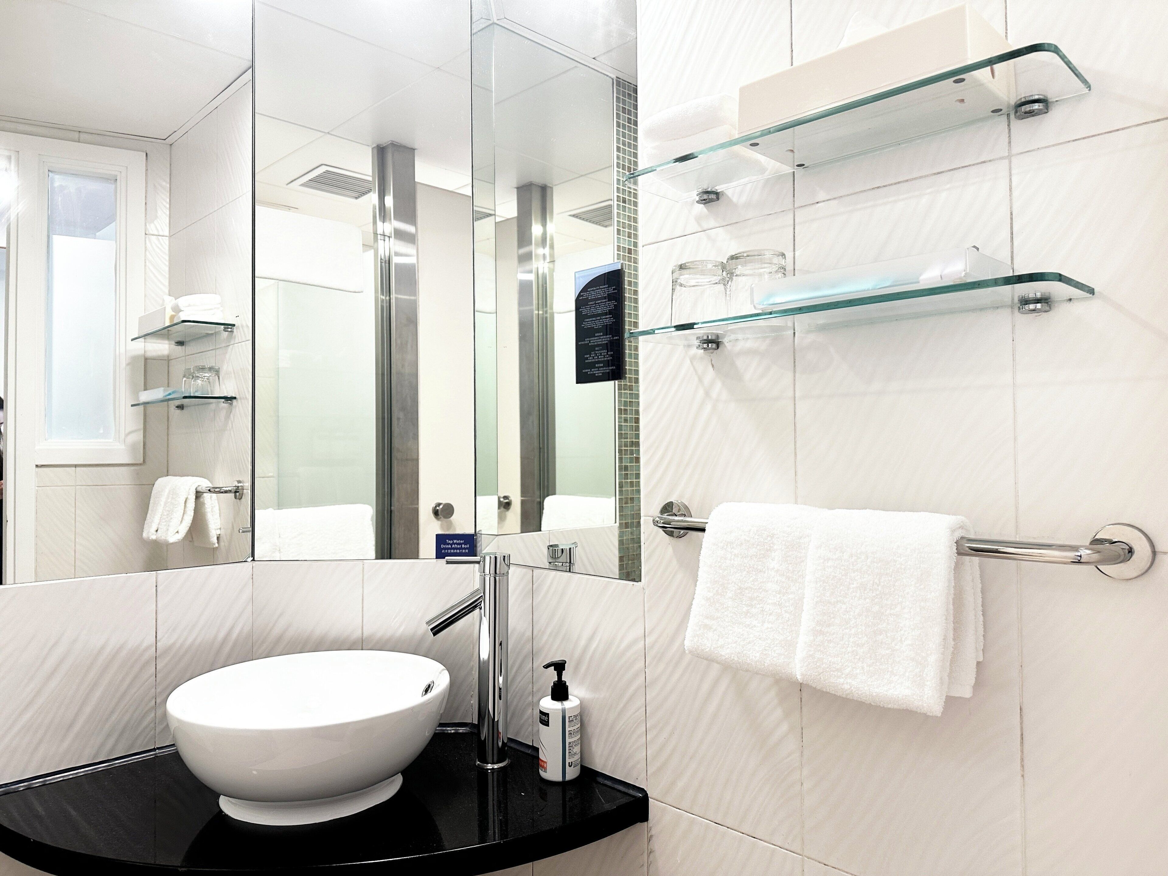 Ein modernes Badezimmer mit einem weißen Waschbecken, einer Duschkabine aus Glas und einer Glasregaleinrichtung.