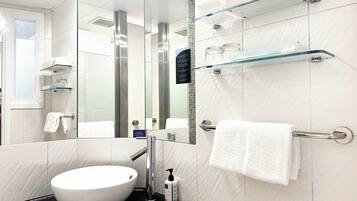 A modern bathroom with a white sink, a glass shower enclosure, and a glass shelf unit.