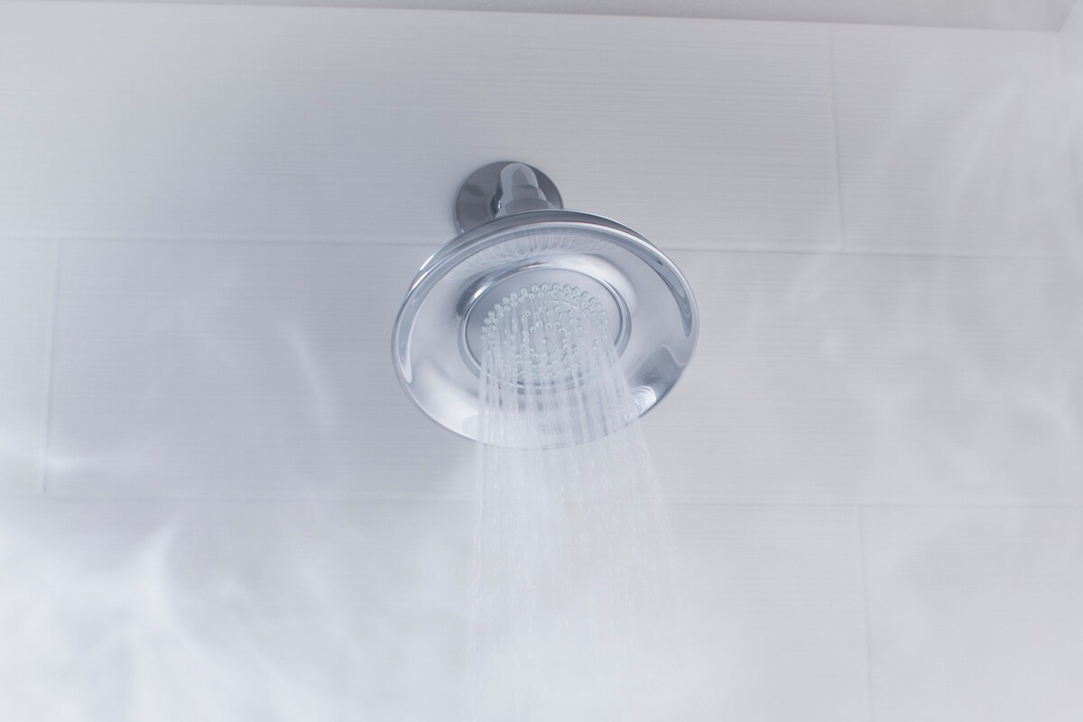 A modern showerhead with water flowing from it, mounted on a white tiled wall.