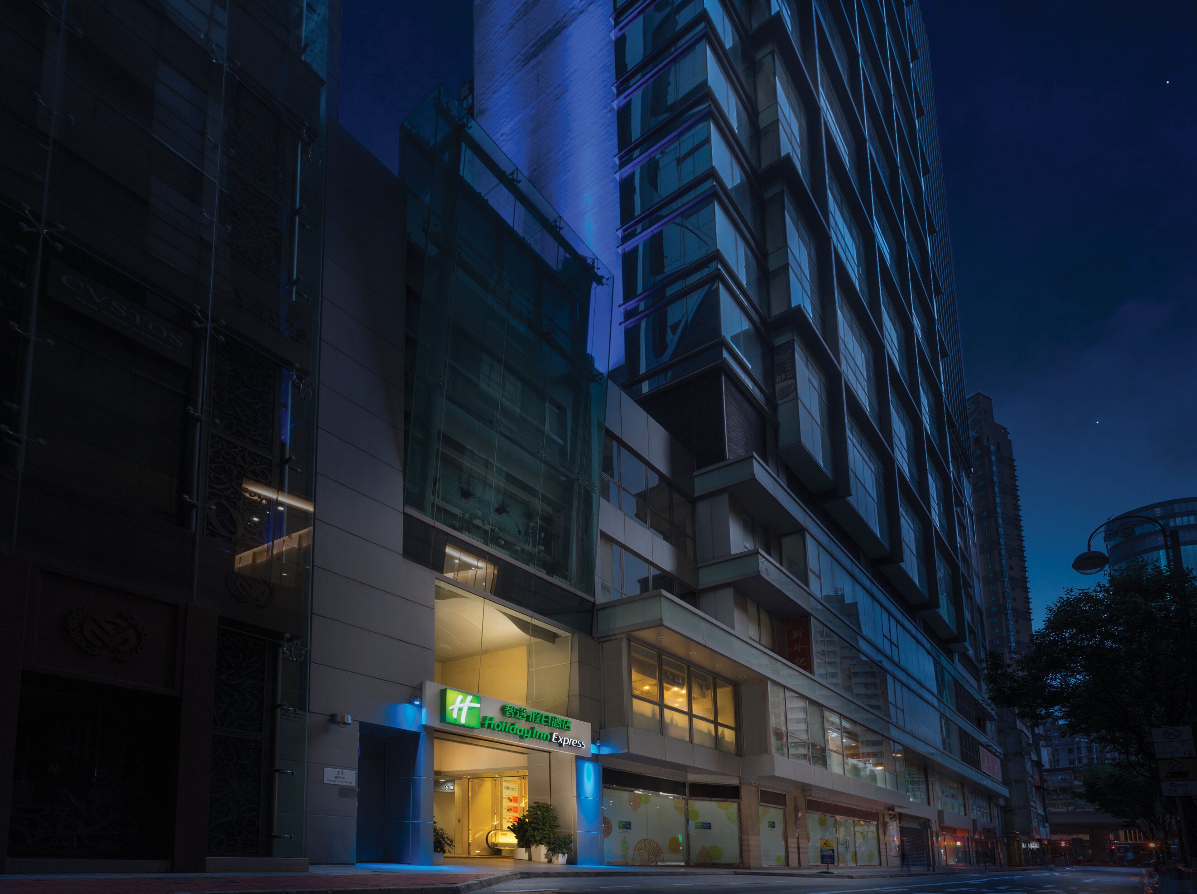 A hotel with a modern facade, large windows, and a prominent green sign.