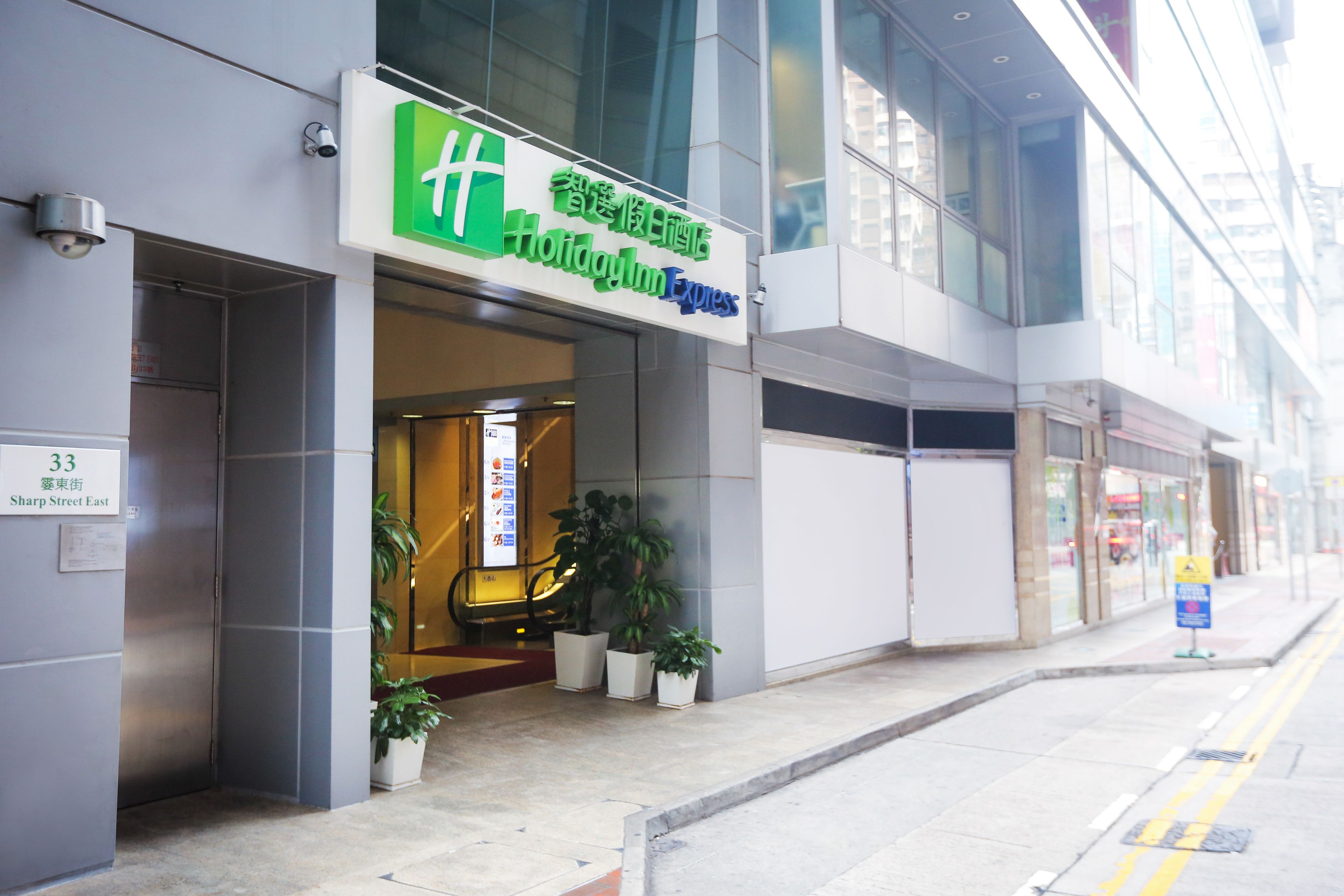 A hotel entrance with a green and white sign, potted plants, and a visible address sign.