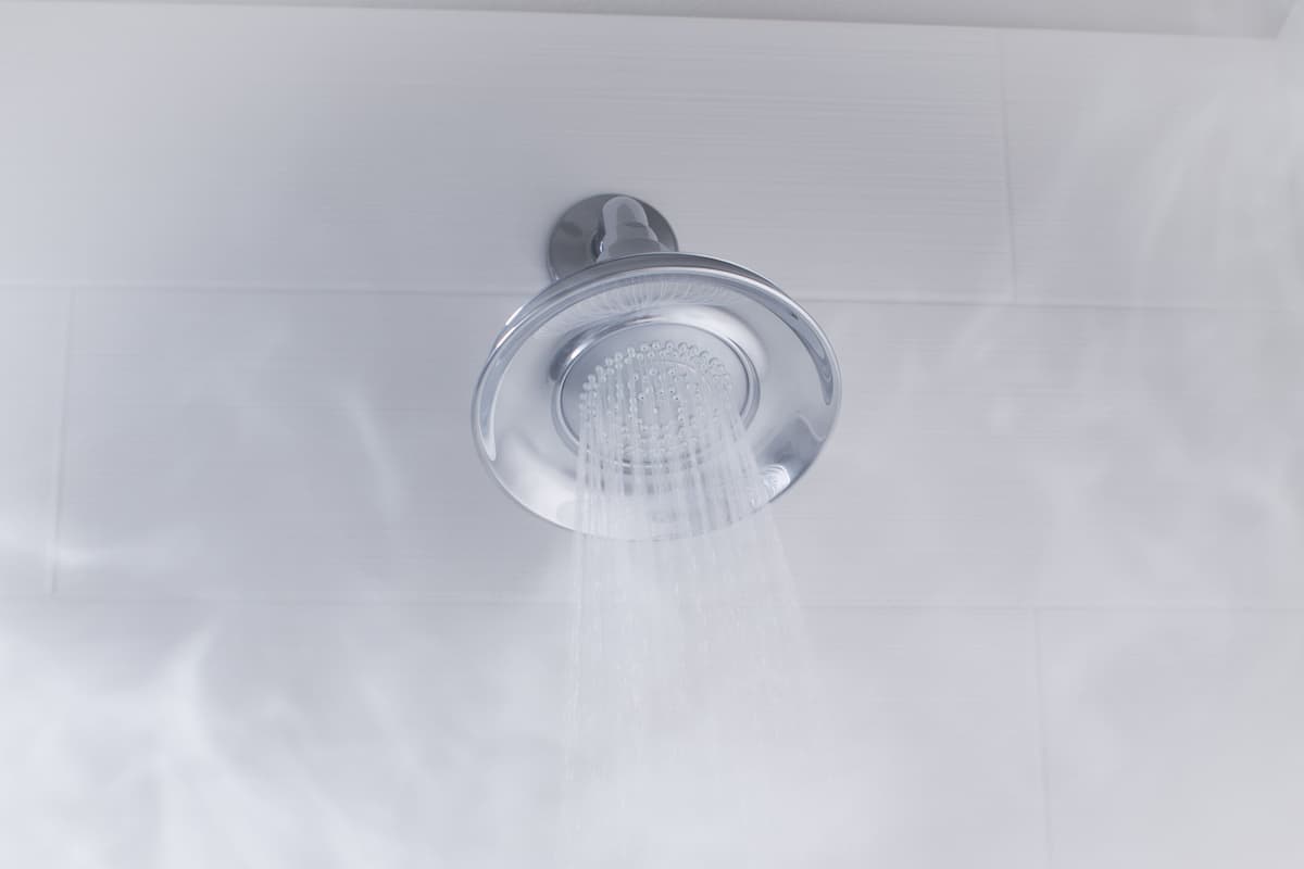 Un cabezal de ducha moderno con agua fluyendo, instalado en una pared de azulejos blancos.