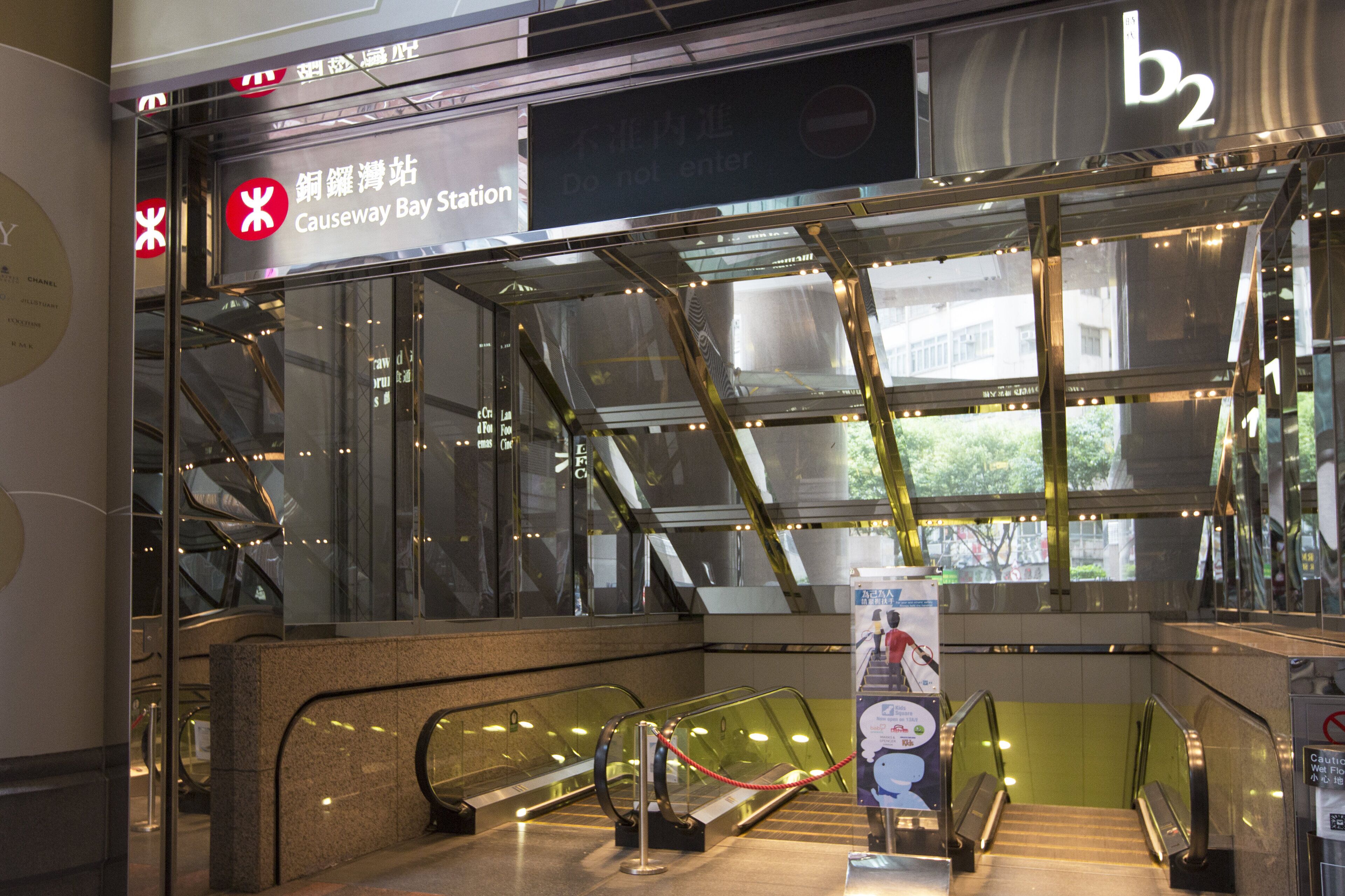 Une station de transport en commun intérieure, dotée d’escalators, de murs en verre et de panneaux indiquant « Station de Causeway Bay ».