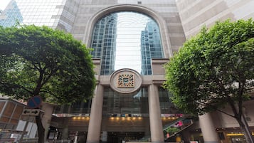 A building with a large arched entrance, a central decorative emblem, and two trees flanking the entrance.