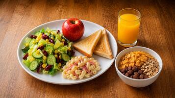 A plate with a salad, apple, macaroni, toast, and a glass of orange juice.