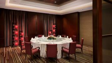 Un salón de conferencias con una mesa redonda, sillas rojas y un centro de mesa floral.
