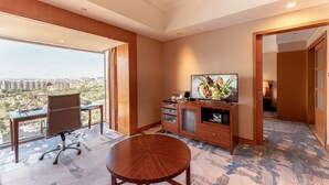 Habitación de hotel con un ventanal grande, una mesa redonda de madera, un escritorio con una silla, un televisor y un armario.