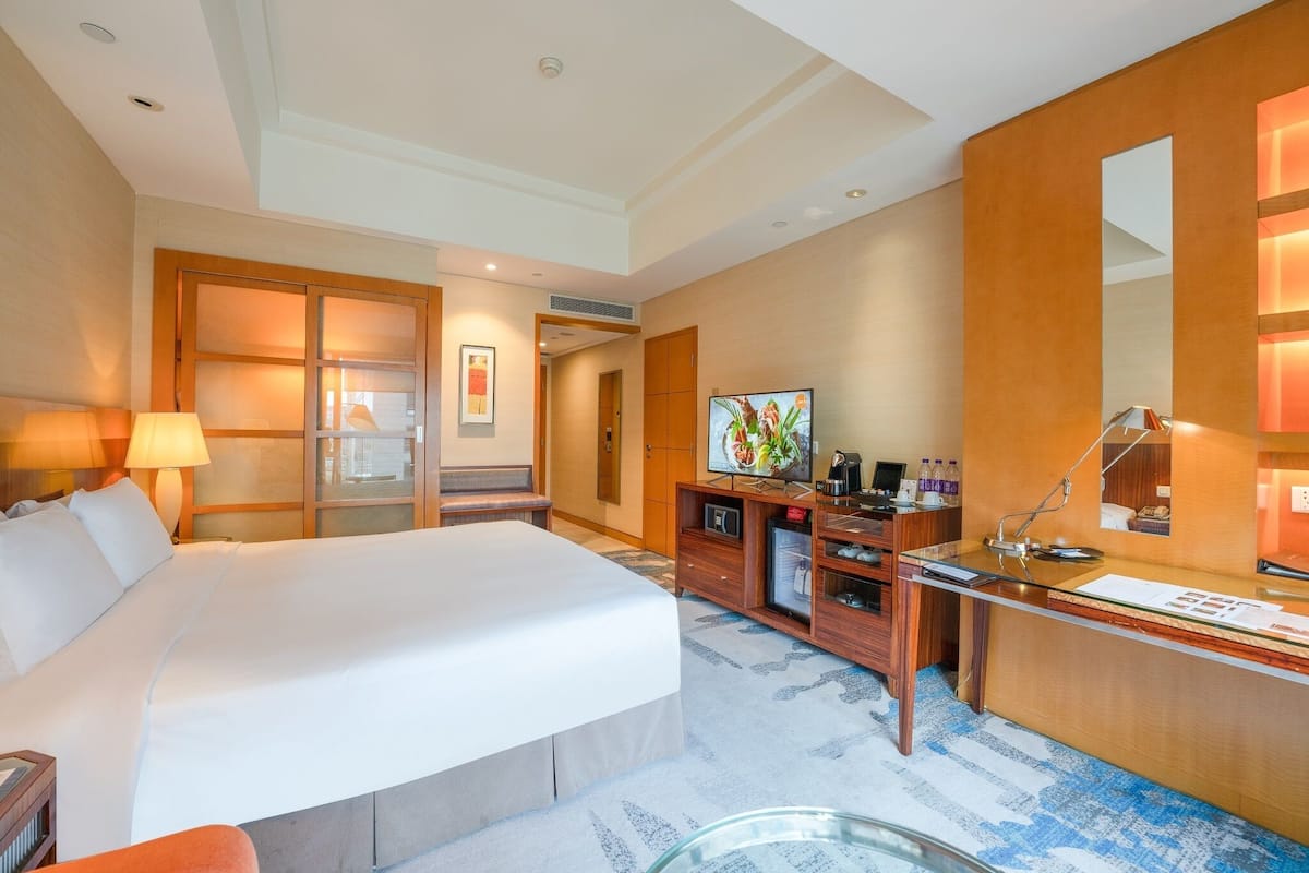A hotel room with a large bed, a desk with a computer, a TV, and a mirror.