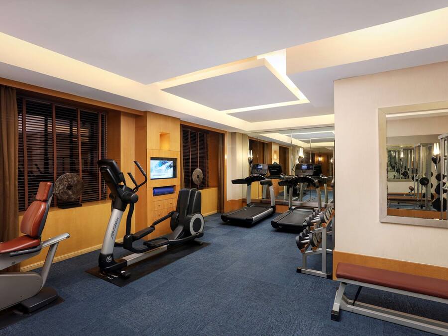 Gimnasio de hotel con máquinas de cardio, bancos de pesas y un espejo.
