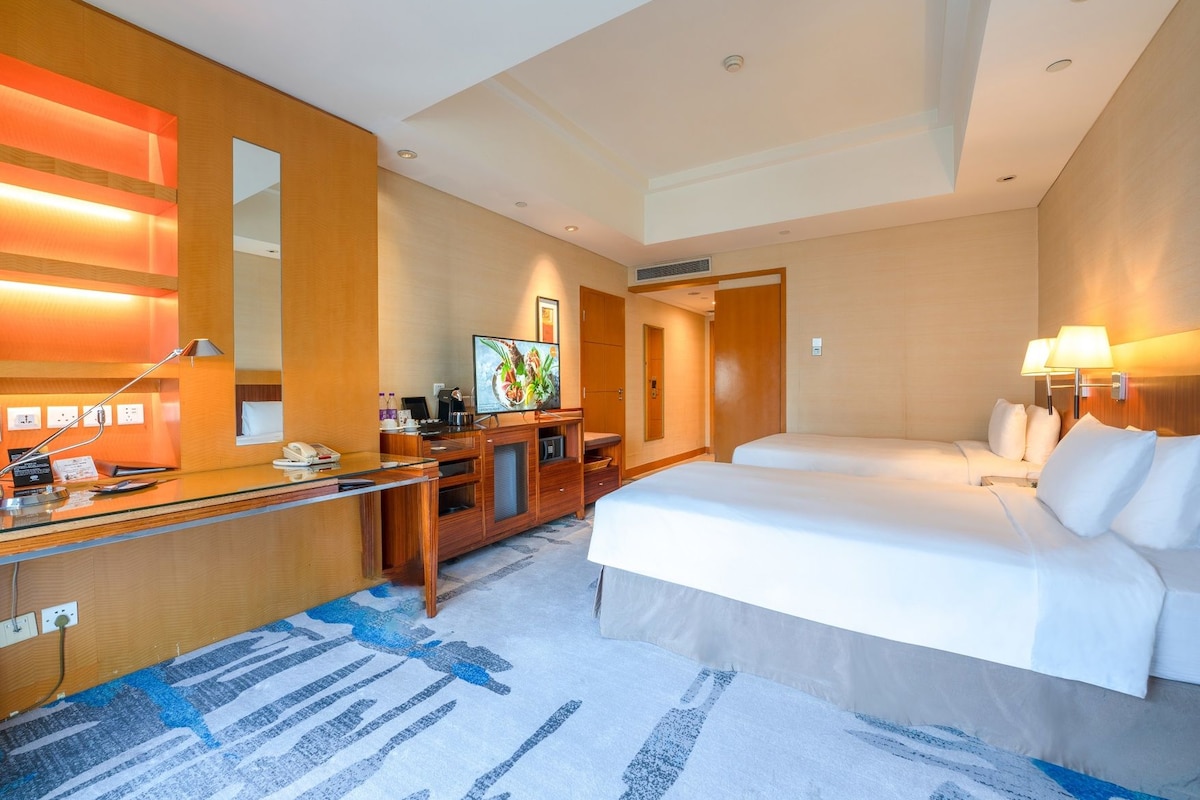 A hotel room with a desk, two beds, a television, and a large mirror.