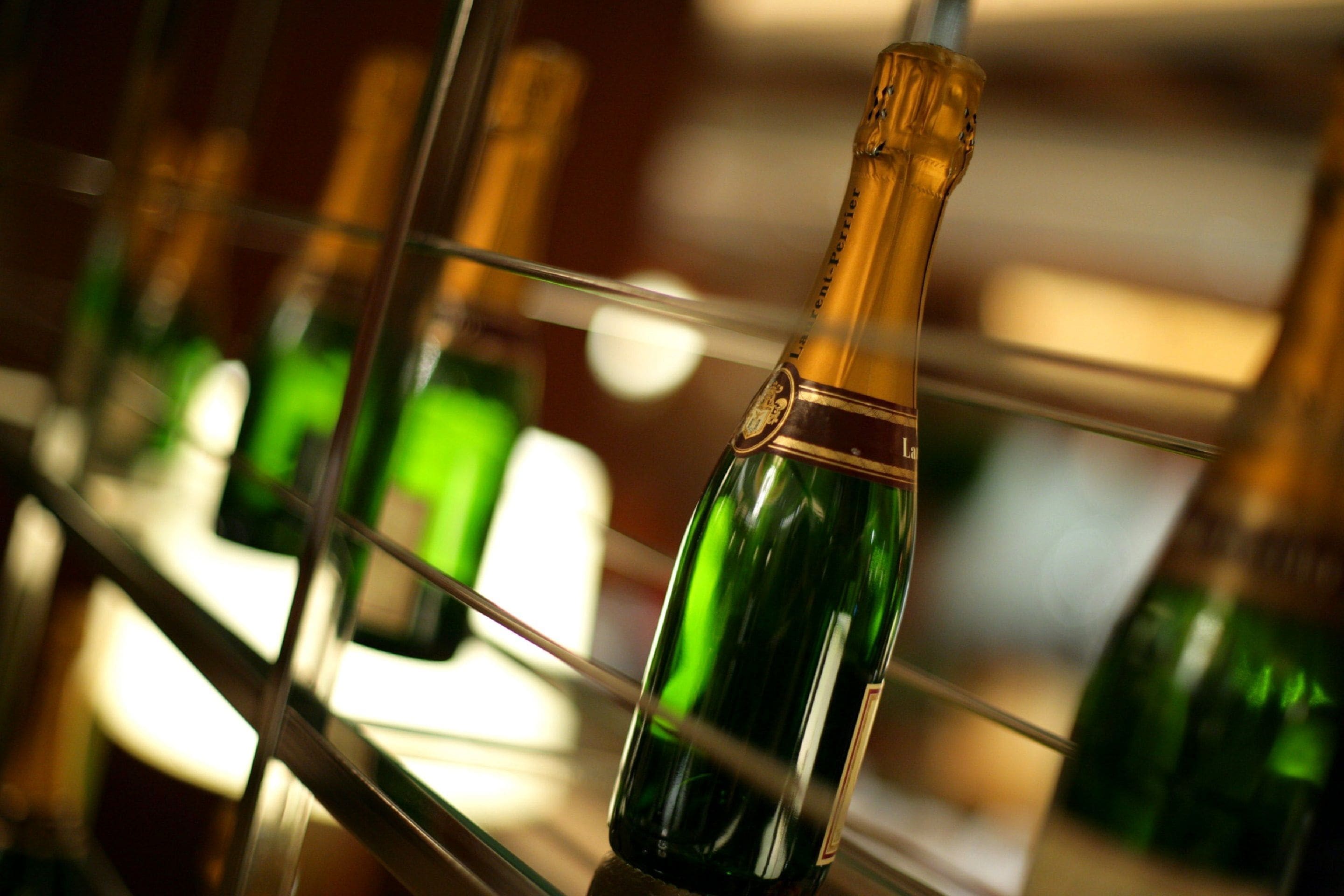 A row of green bottles with gold foil, likely containing champagne, displayed on a metal rack.