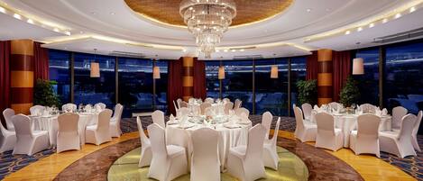 Un salón de banquetes con mesas redondas, sillas blancas y una gran araña.