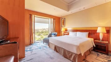 A hotel room with a large bed, a television, a chair, a desk, and a window with a city view.
